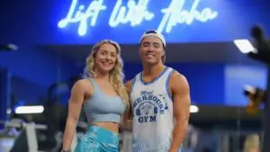 Two members smiling under the Lift With Aloha neon sign at Maui Powerhouse Gym