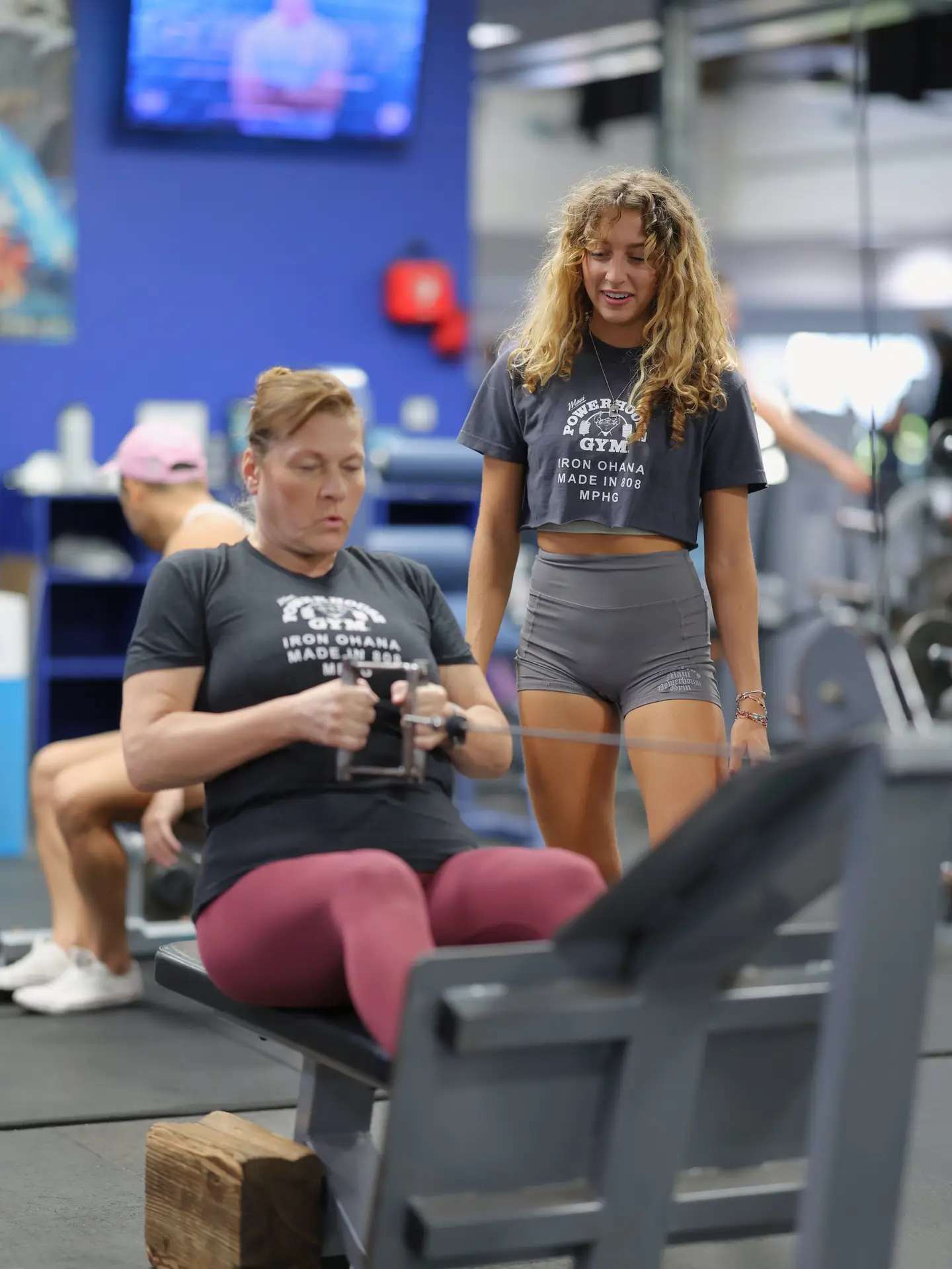 A woman using gym equipment with another woman nearby to help at Maui Powerhouse Gym